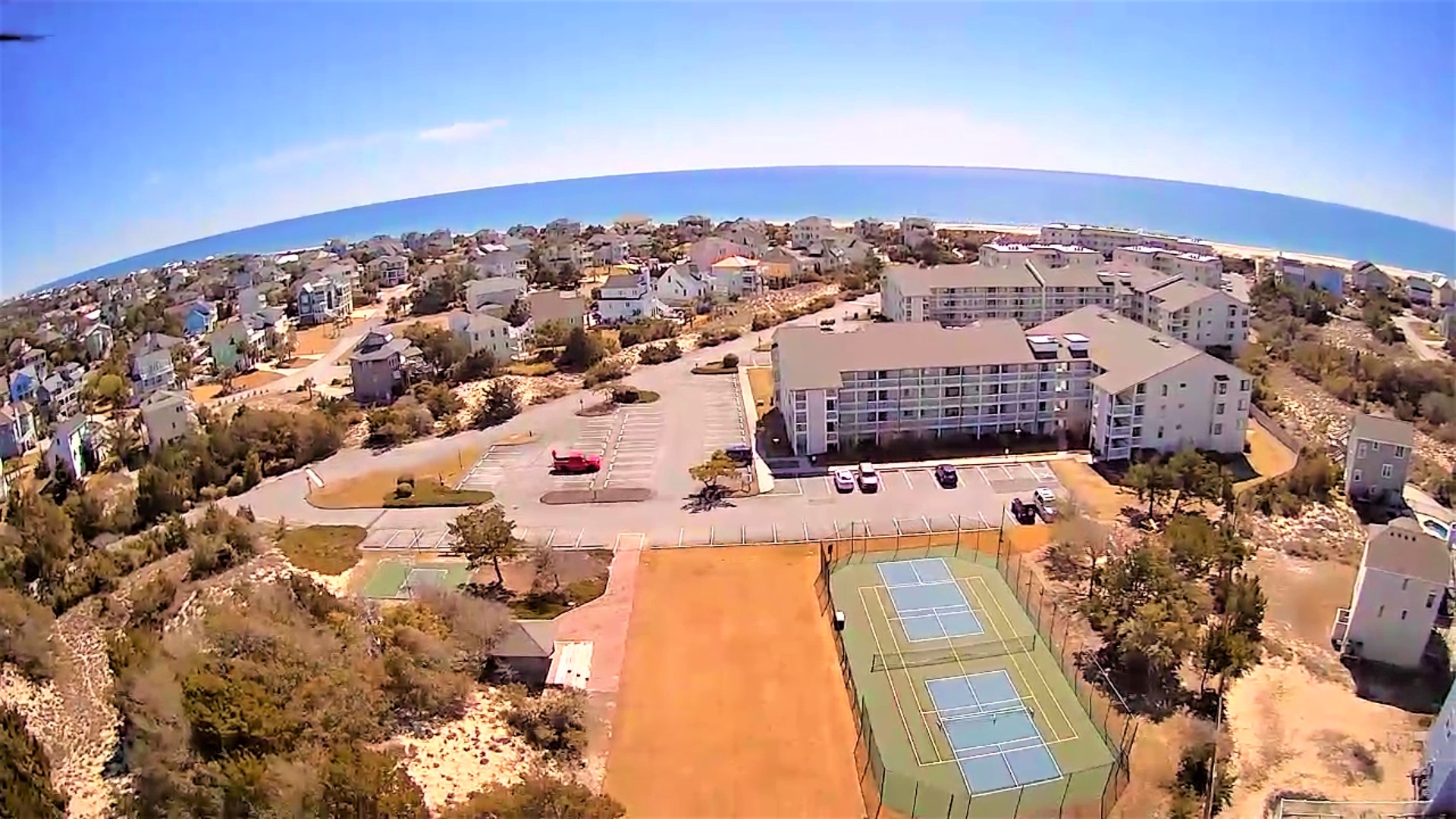 Aerial view of coastal resort property with tennis courts, surrounded by Mediterranean-style buildings near pristine beaches.