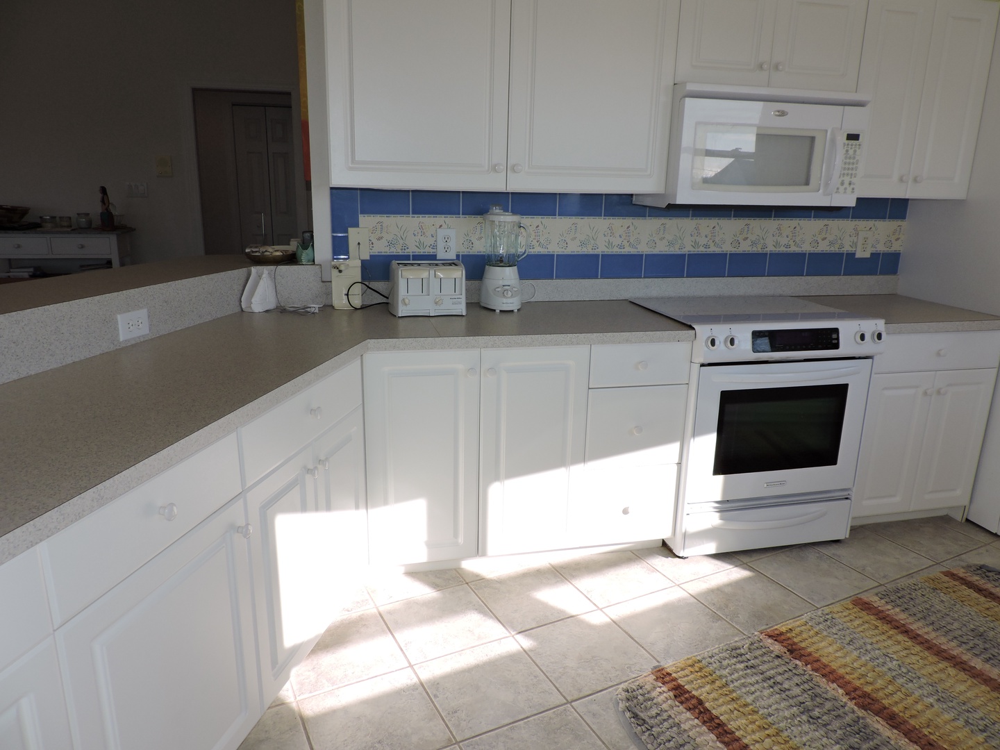 Your bright, fully-equipped kitchen awaits with white cabinets, modern appliances, and cheerful blue tile accents—perfect for preparing meals.