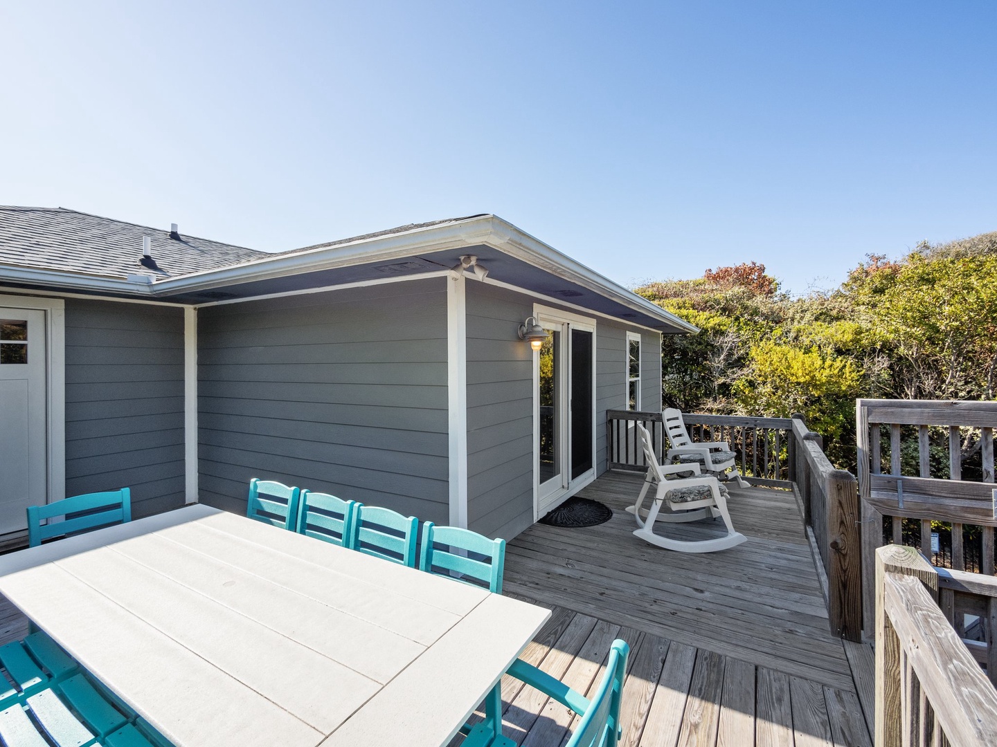 Spacious deck with dining table and rocking chair where you can enjoy meals outdoors and peaceful moments surrounded by coastal greenery.