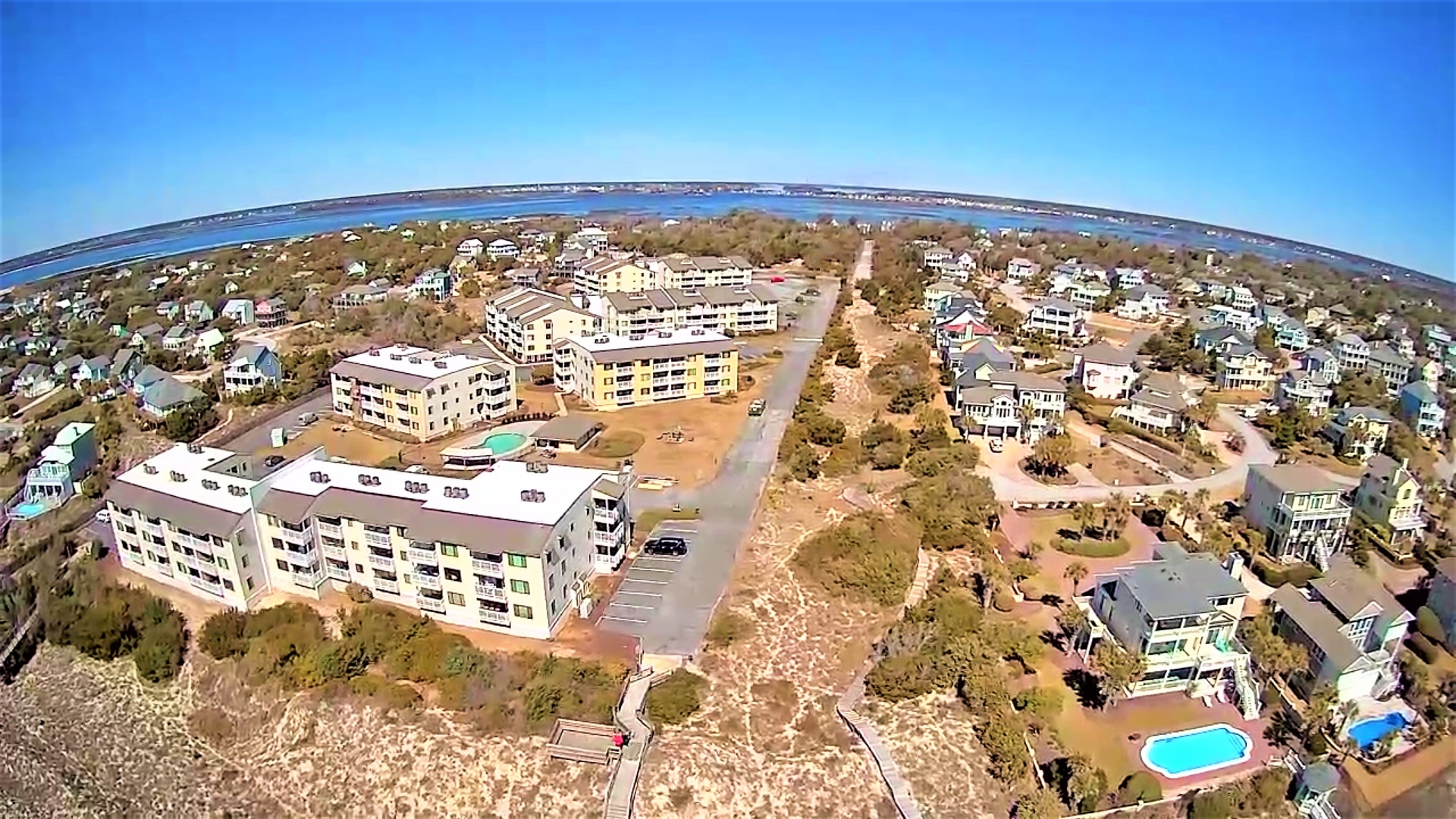 Aerial view of beachfront community featuring modern vacation homes and condominiums nestled among natural dunes, just steps from pristine coastline.