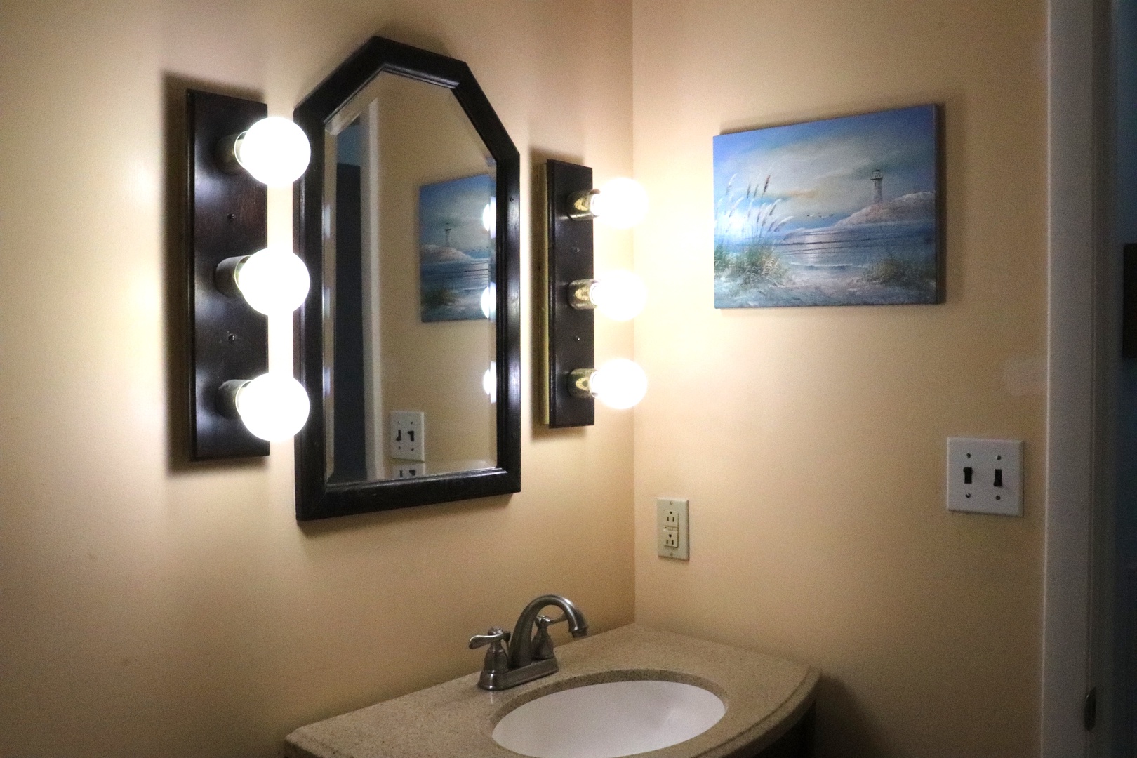 Your bathroom features bright vanity lighting, a stylish mirror, and coastal artwork that brings the beach right to your doorstep.