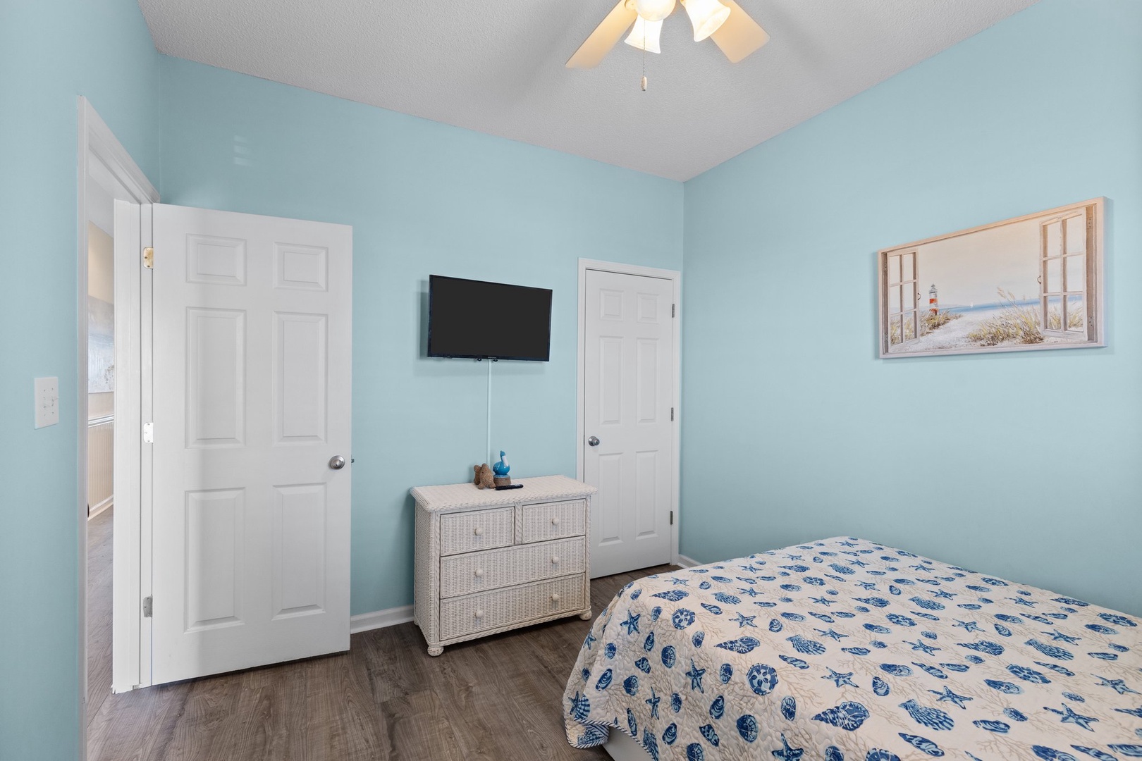 Relax in your coastal-themed bedroom with soothing blue walls, comfortable bedding, and modern amenities including flat-screen TV and ceiling fan.