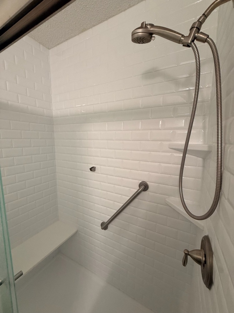 Step into a pristine walk-in shower with classic white subway tile and a handheld showerhead for your comfort. A safety grab bar adds thoughtful accessibility for all guests.
