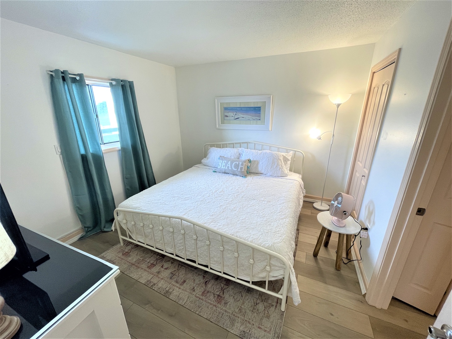 Your serene bedroom offers a comfortable white metal bed with crisp linens, calming coastal touches, and natural light from your private window.