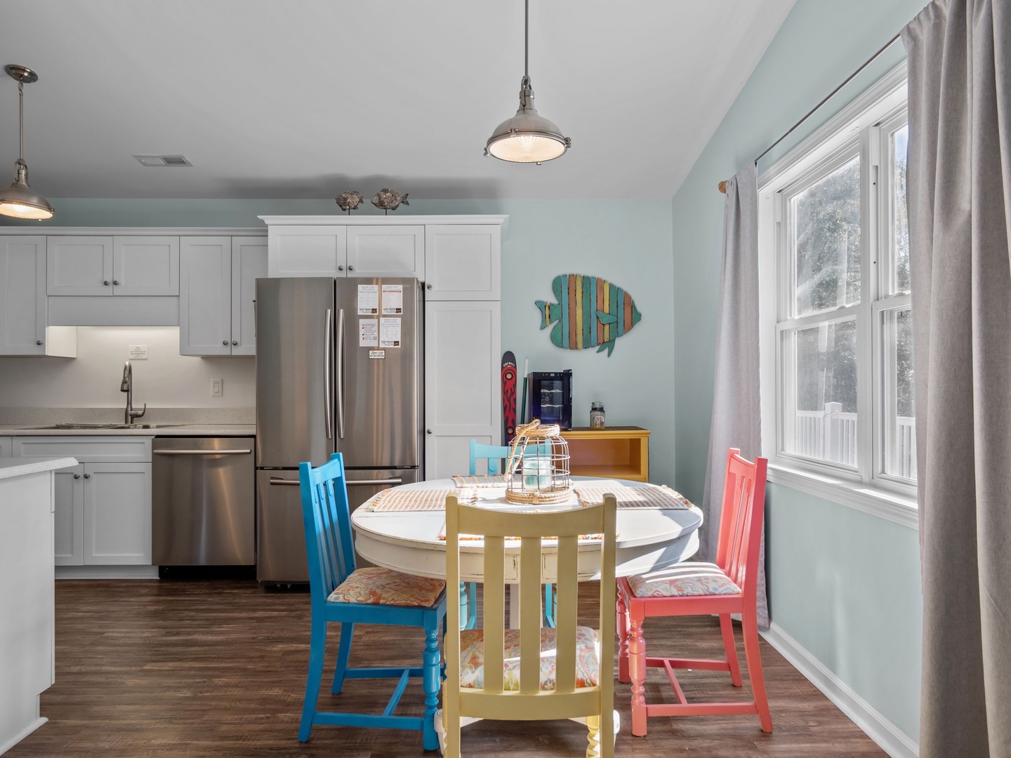 Your bright kitchen flows into a cheerful dining space with colorful chairs and coastal touches—perfect for family meals and morning coffee.