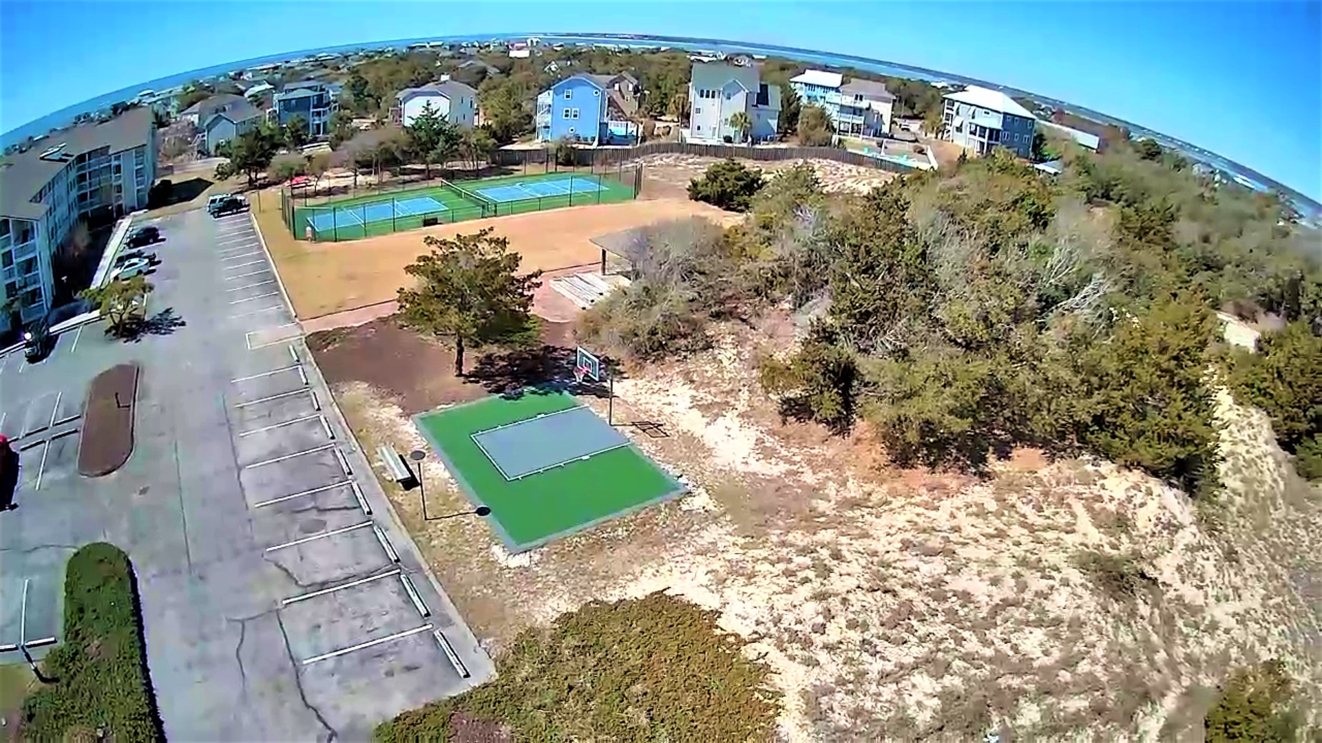 Aerial view of coastal community featuring tennis courts and recreational facilities among residential homes and natural landscape.
