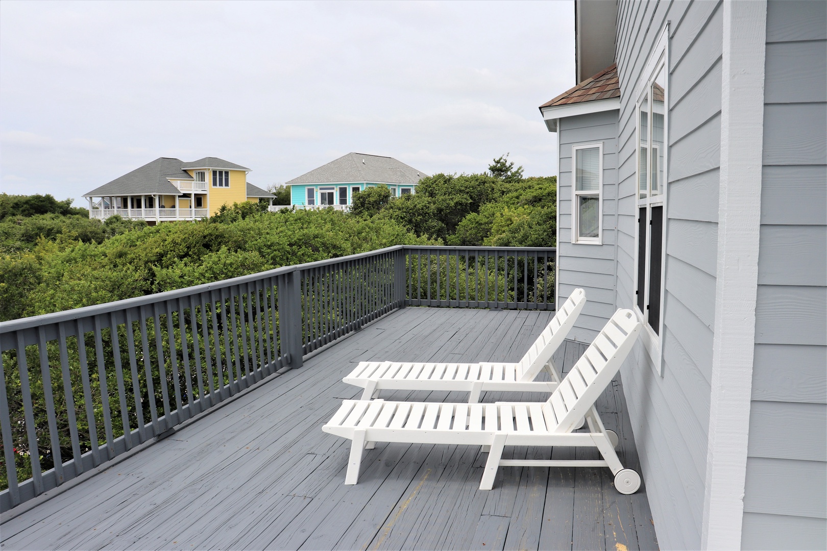 Spacious deck with comfortable lounge chairs overlooking colorful coastal neighborhood through lush greenery.