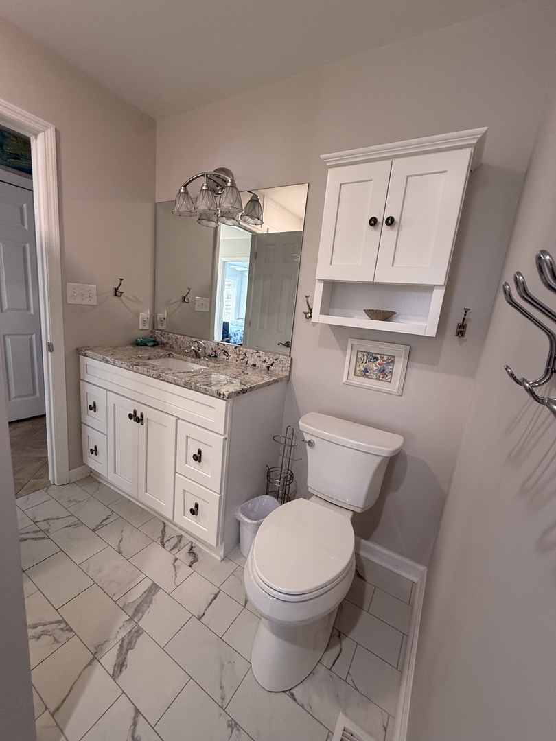 Refresh in your private bathroom with elegant white cabinetry, marble countertops, herringbone tile floors, and a sleek walk-in shower—designed for comfort and style during your stay.