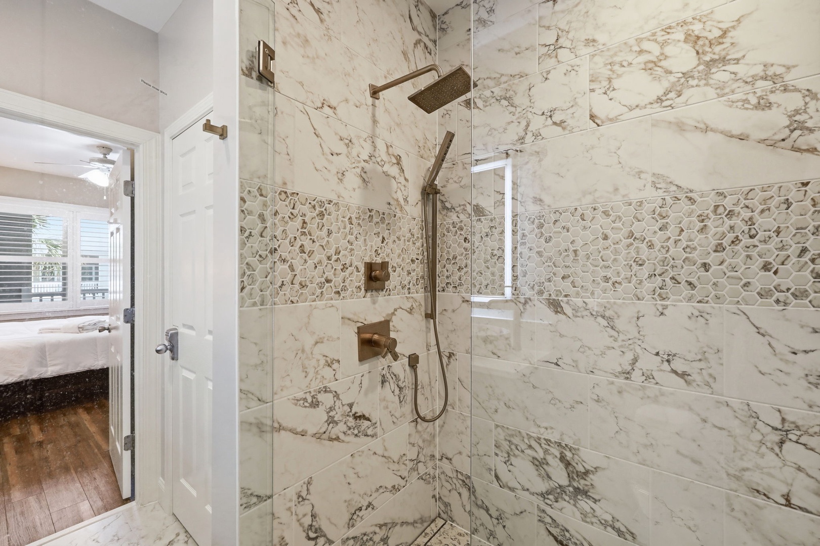 Step into your luxurious walk-in shower, beautifully appointed with marble-inspired tile and elegant gold fixtures. The rainfall showerhead and handheld spray promise a spa-like retreat after a day of exploring.