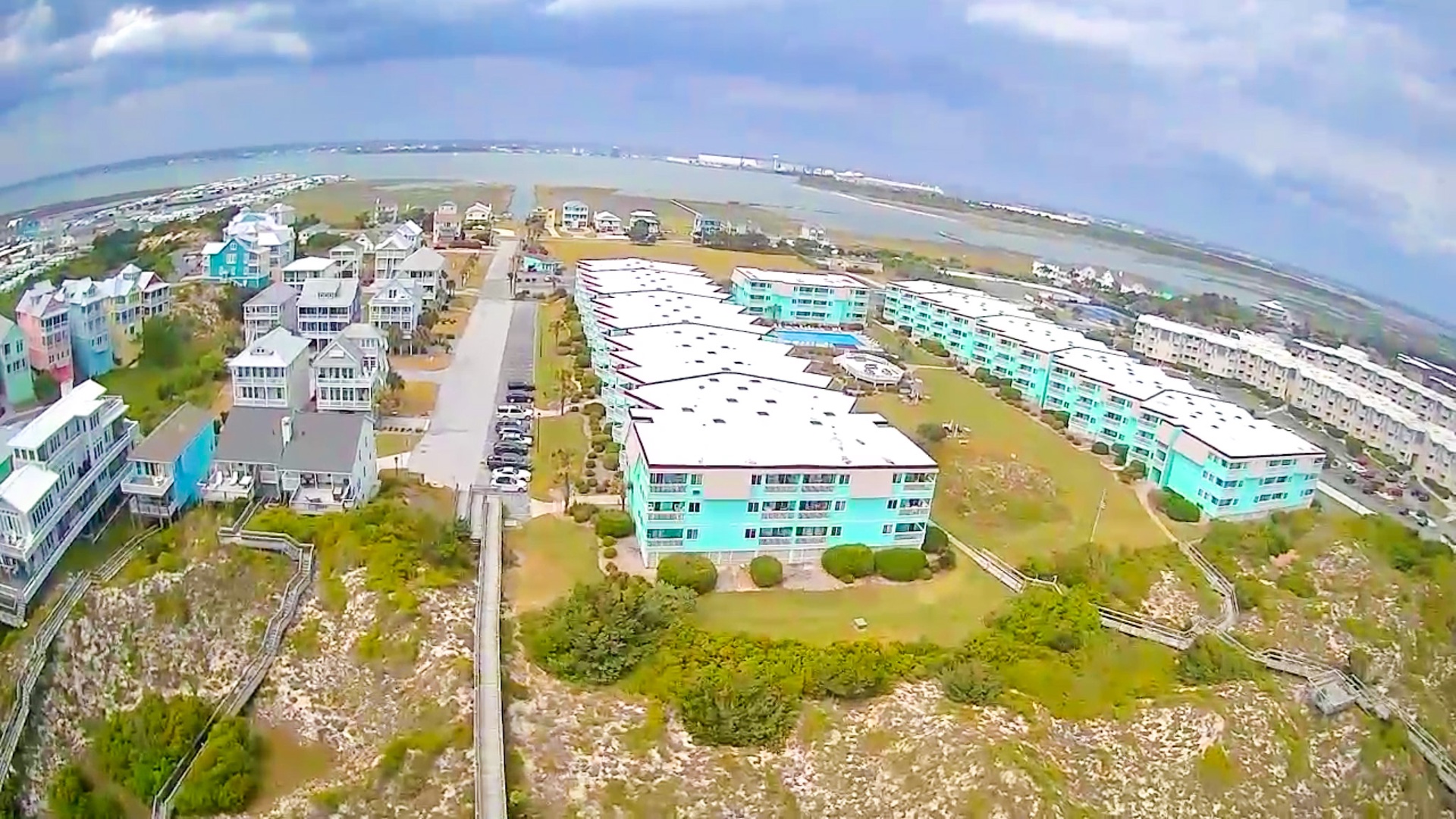 Aerial view of coastal vacation rentals featuring distinctive turquoise buildings amid oceanfront community with beach access and scenic waterfront setting.
