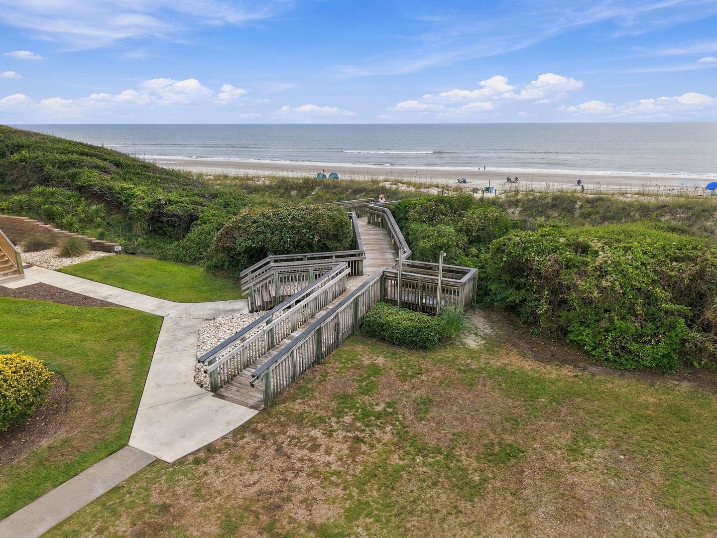The property features direct beach access via a private boardwalk, leading through dunes and coastal greenery to a wide stretch of pristine sandy shoreline where the Atlantic meets the sky.