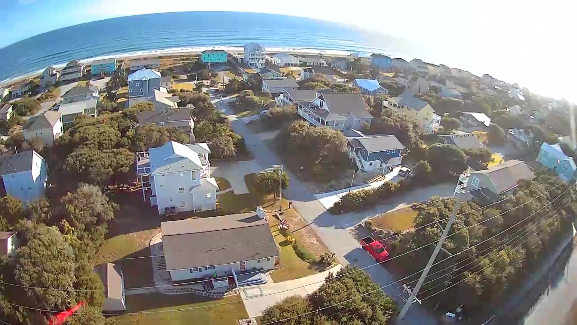 Coastal community with beach houses nestled among mature trees, just steps from the sandy shoreline and ocean waves.