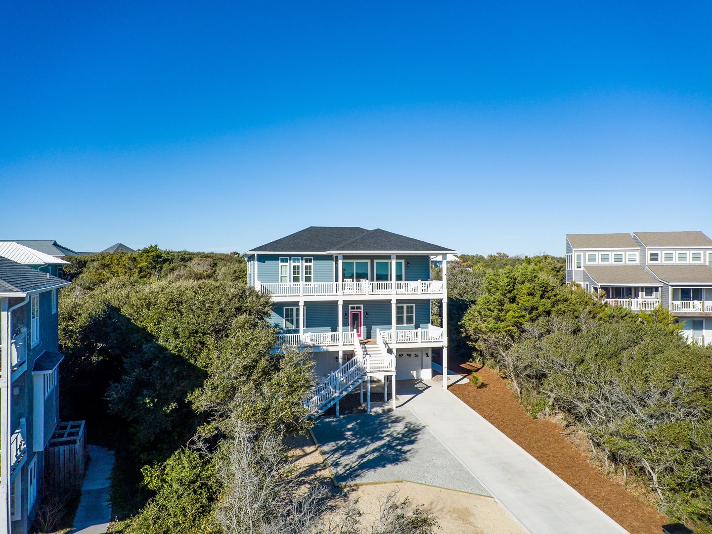 Coastal vacation home nestled among mature trees in a peaceful residential neighborhood, featuring multiple levels and wraparound porches.