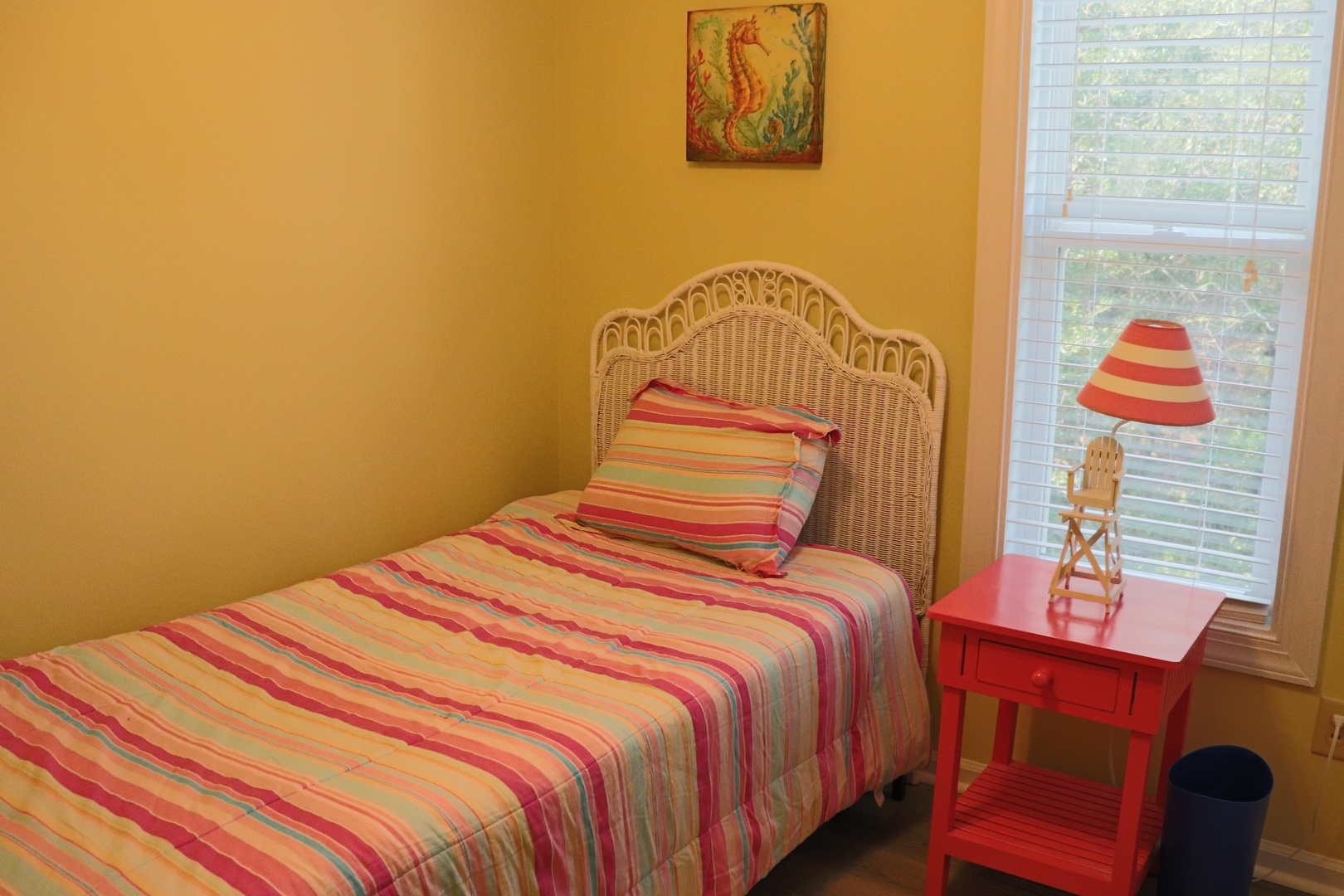 Rest peacefully in your cozy bedroom with vibrant striped linens and charming wicker headboard, bathed in natural light.
