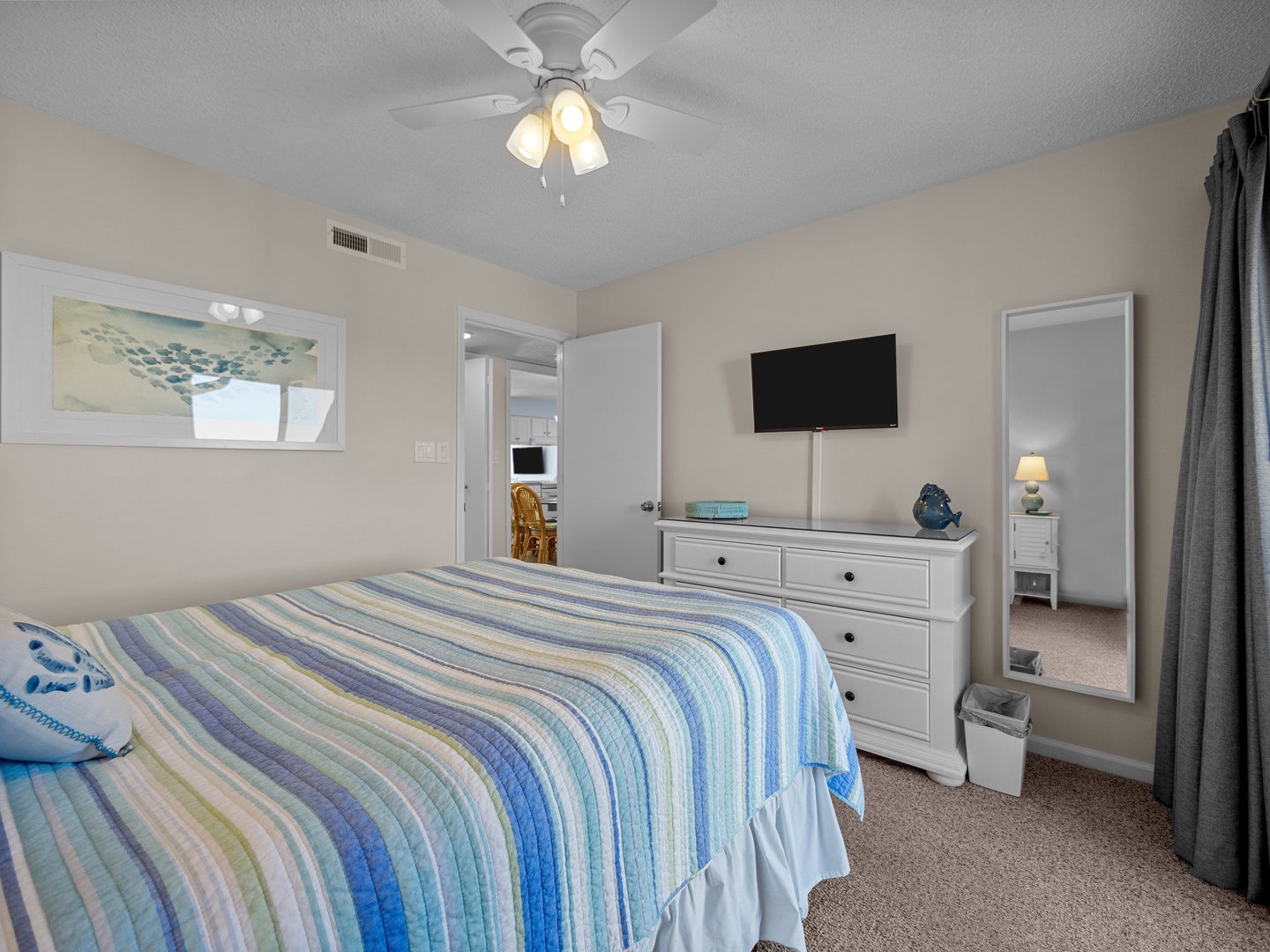 Relax in your peaceful bedroom featuring coastal colors, comfortable bedding, and modern amenities including a wall-mounted TV and ceiling fan for your comfort.