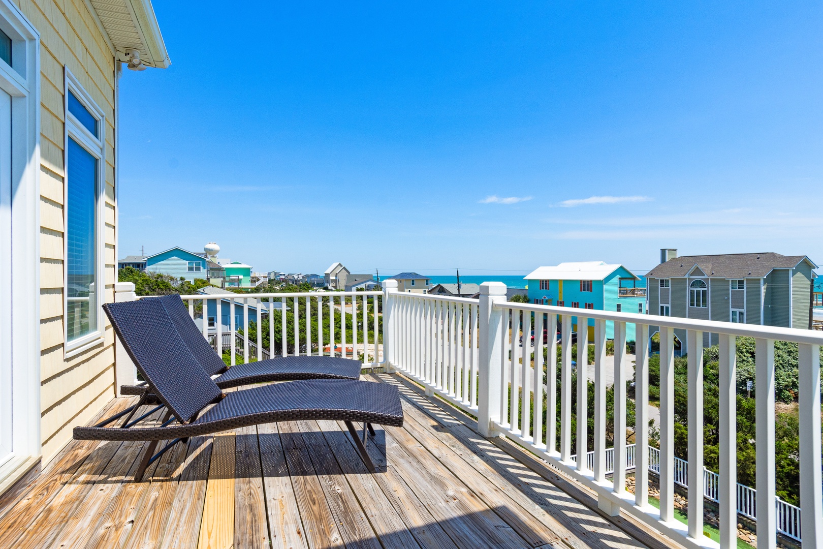 Bright coastal views stretch beyond this private deck, featuring colorful beach houses and blue skies perfect for peaceful moments.