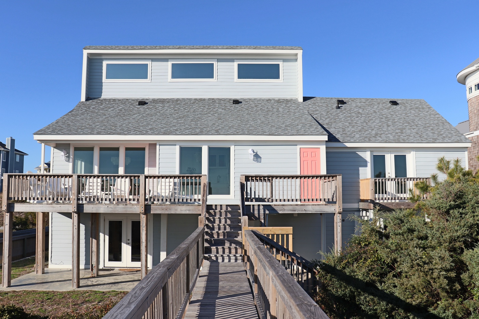 Coastal beach house featuring elevated design with wraparound decks and boardwalk access under clear blue skies.