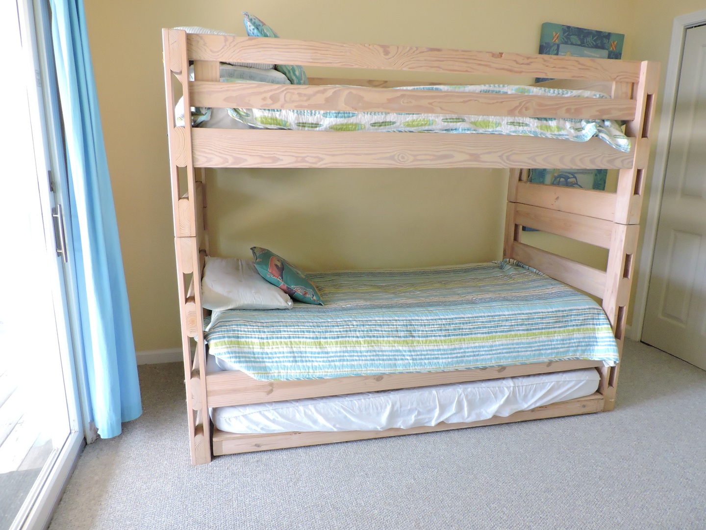 Perfect for families, this cozy bunk bed setup with trundle sleeps three comfortably in cheerful blue and green linens.