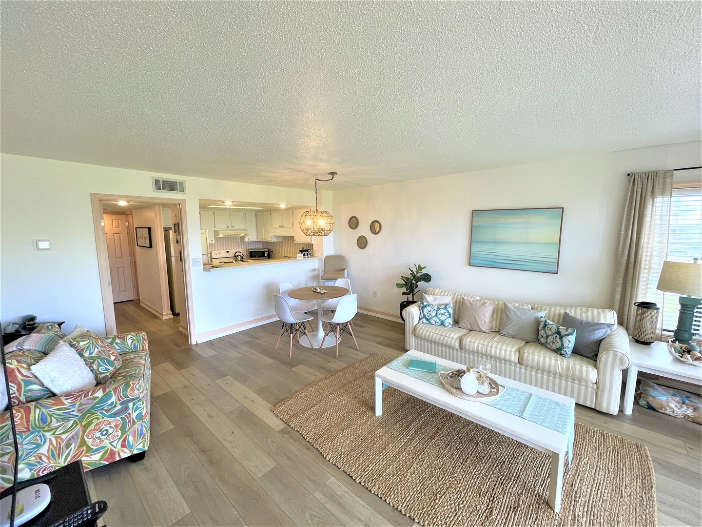 Relax in your bright, coastal-themed living space featuring comfortable seating, ocean-inspired artwork, and an open layout connecting to your fully equipped kitchen.