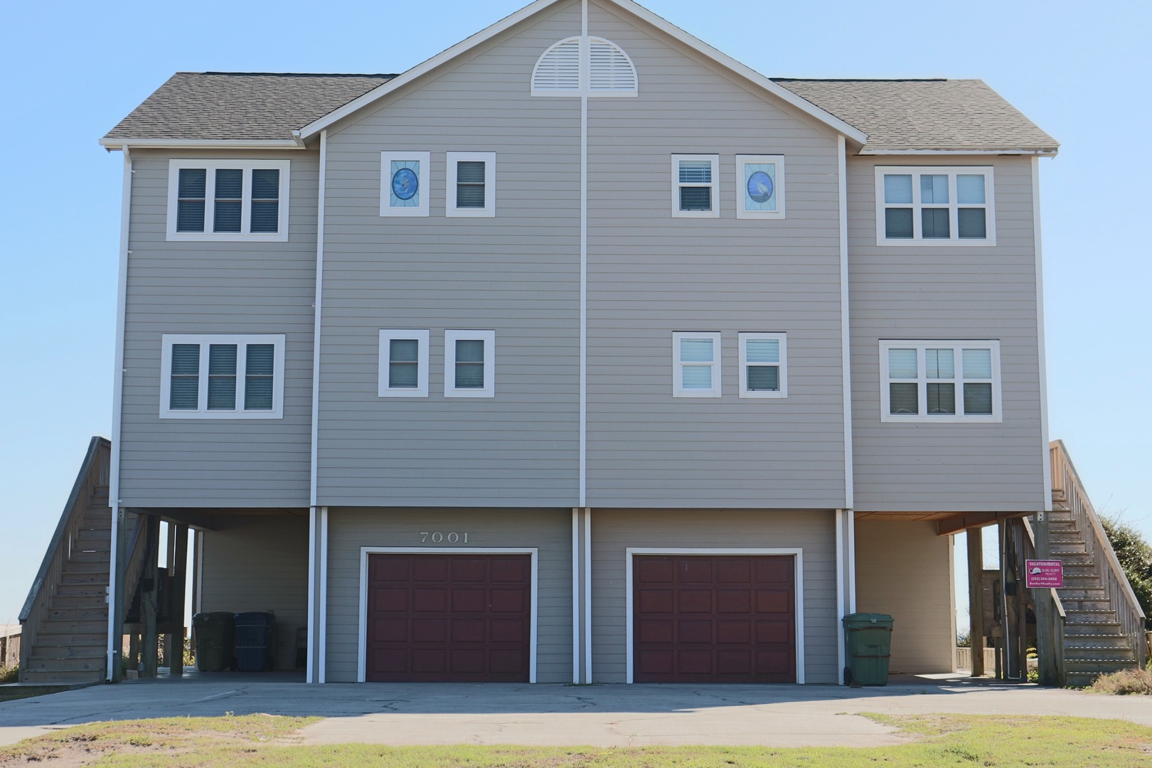 A coastal vacation home elevated on stilts with ground-level garage parking and stairs leading to the main living areas.