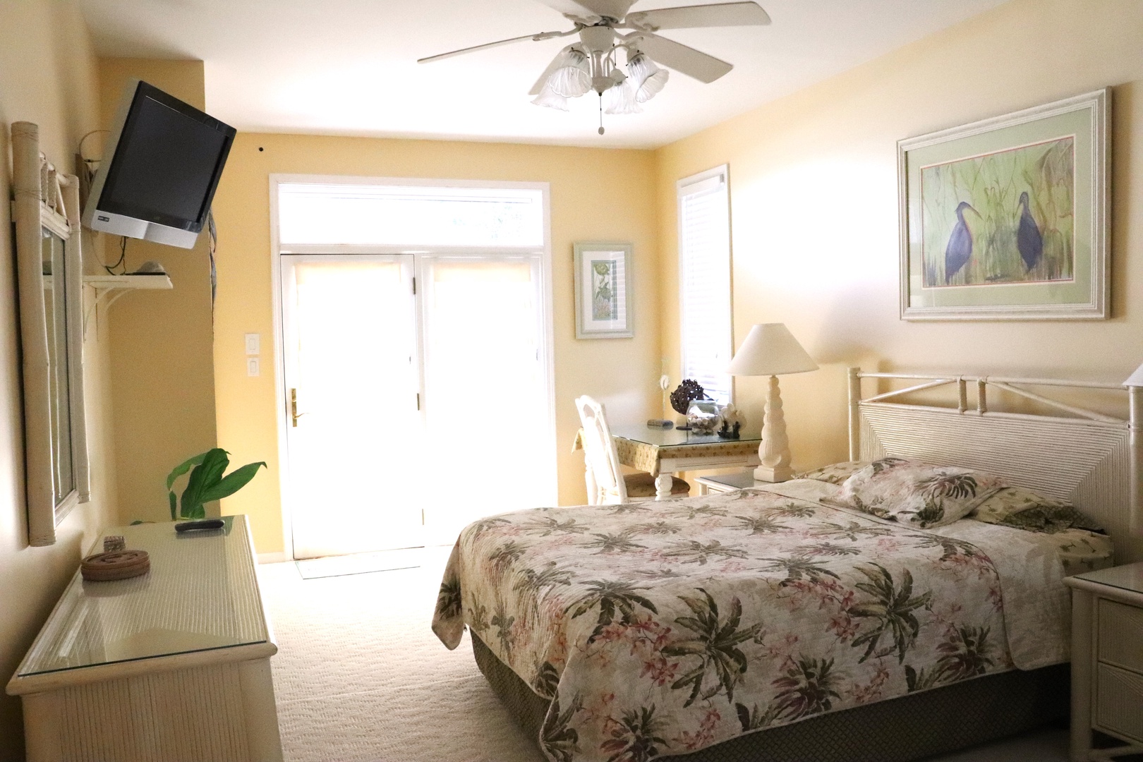 Relax in this bright, tropical-themed bedroom with comfortable bedding, ceiling fan, and TV for your entertainment.