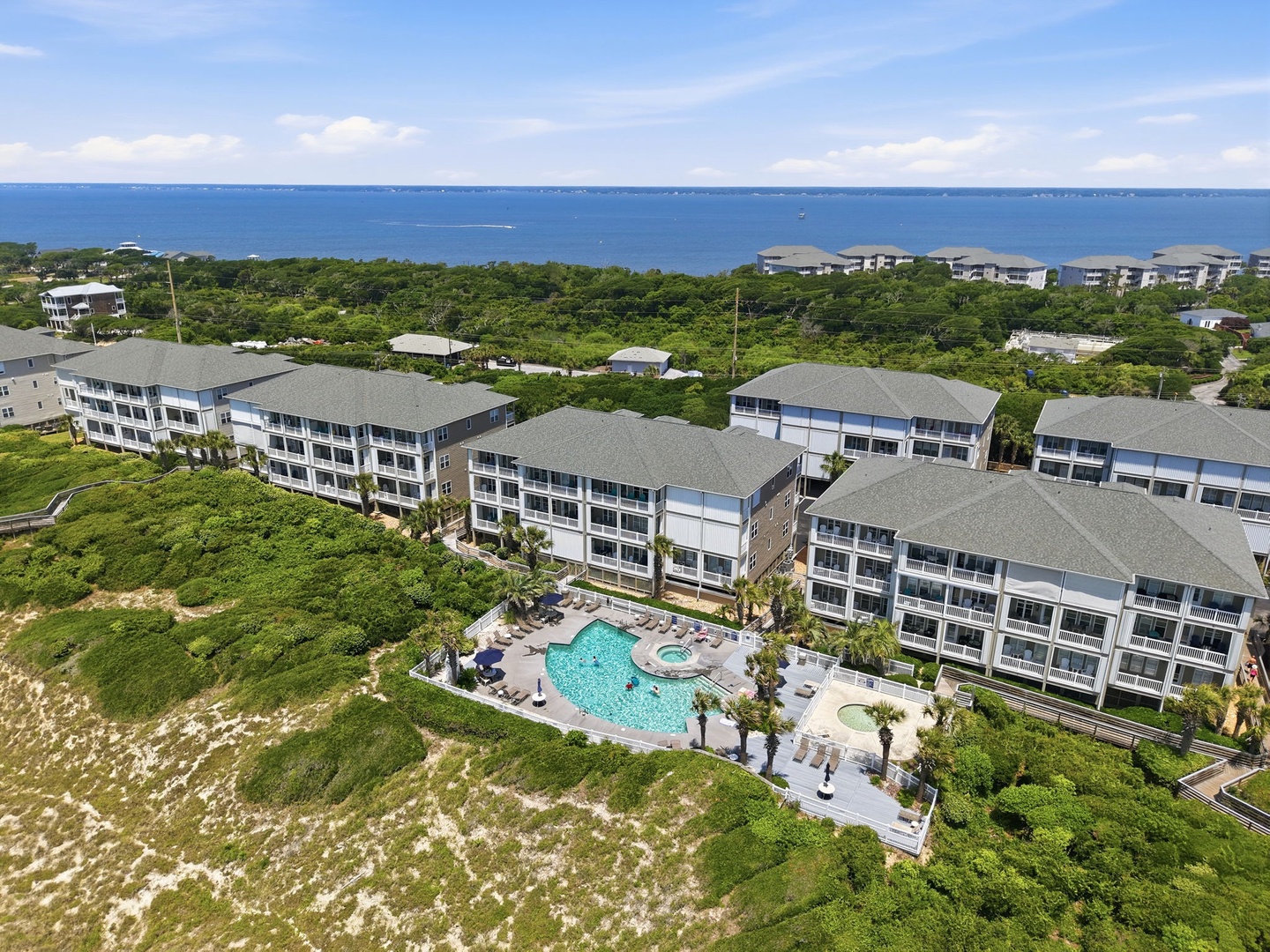 Aerial view of the multi-building vacation complex featuring coastal landscaping, resort-style pool facilities, and surrounding natural vegetation near the ocean shore.