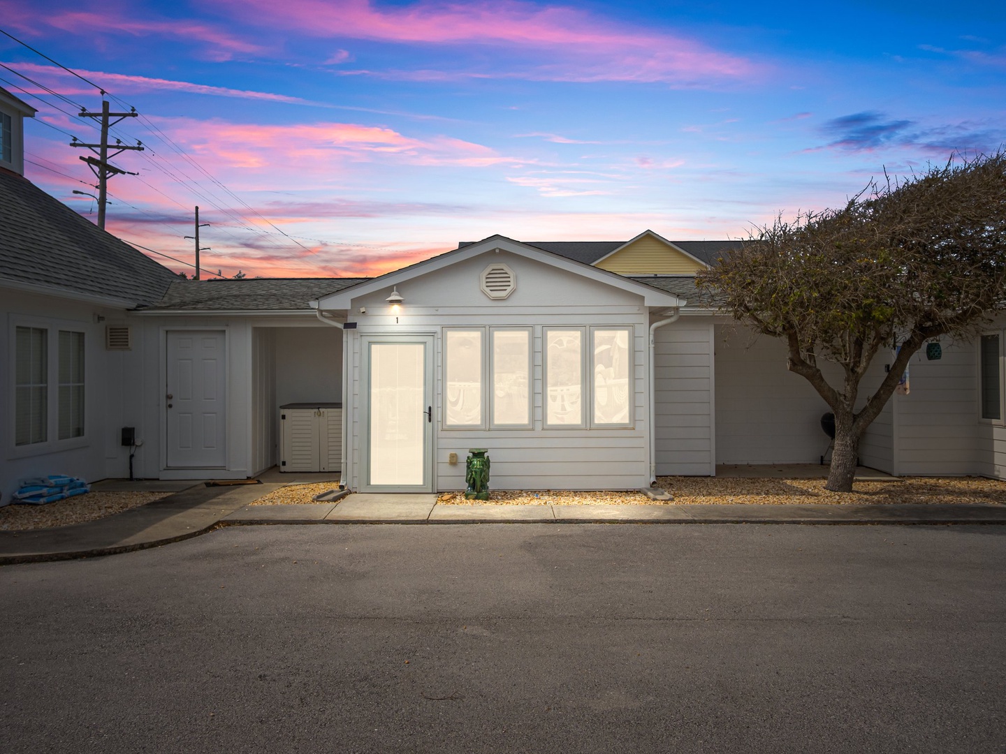 A charming coastal cottage with dramatic sunset skies painting the neighborhood in warm hues during arrival.