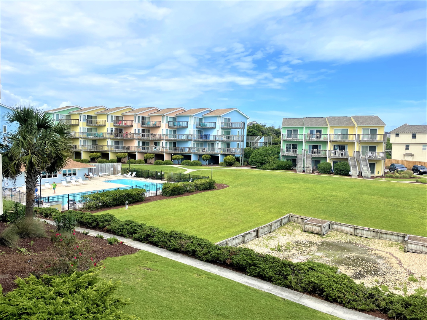 Colorful beachside resort with swimming pool, lush grounds, and multi-story vacation rental buildings offering coastal charm and relaxation.