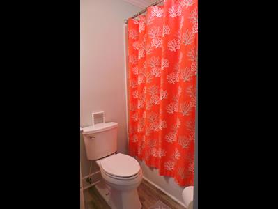 Your private bathroom features a fresh, clean toilet with vibrant coral-patterned shower curtain adding warmth to the space.