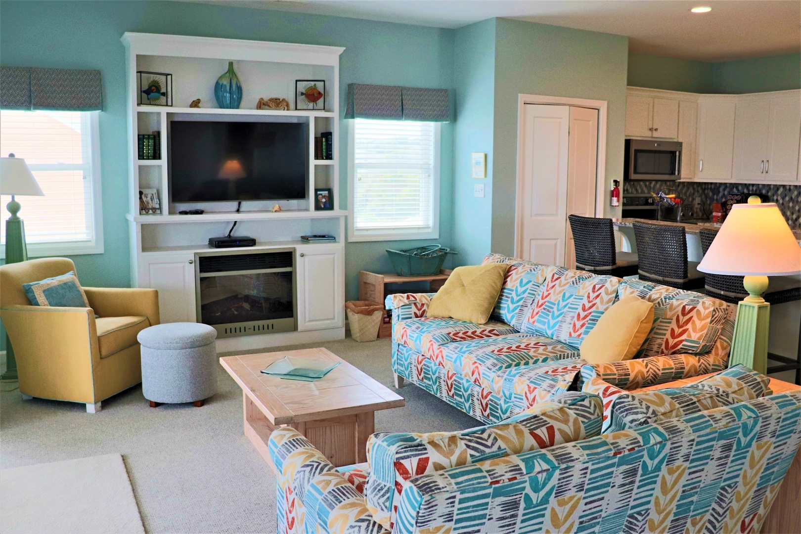 Relax in your bright coastal living space with colorful patterned seating, built-in entertainment center, and open kitchen perfect for family gatherings.