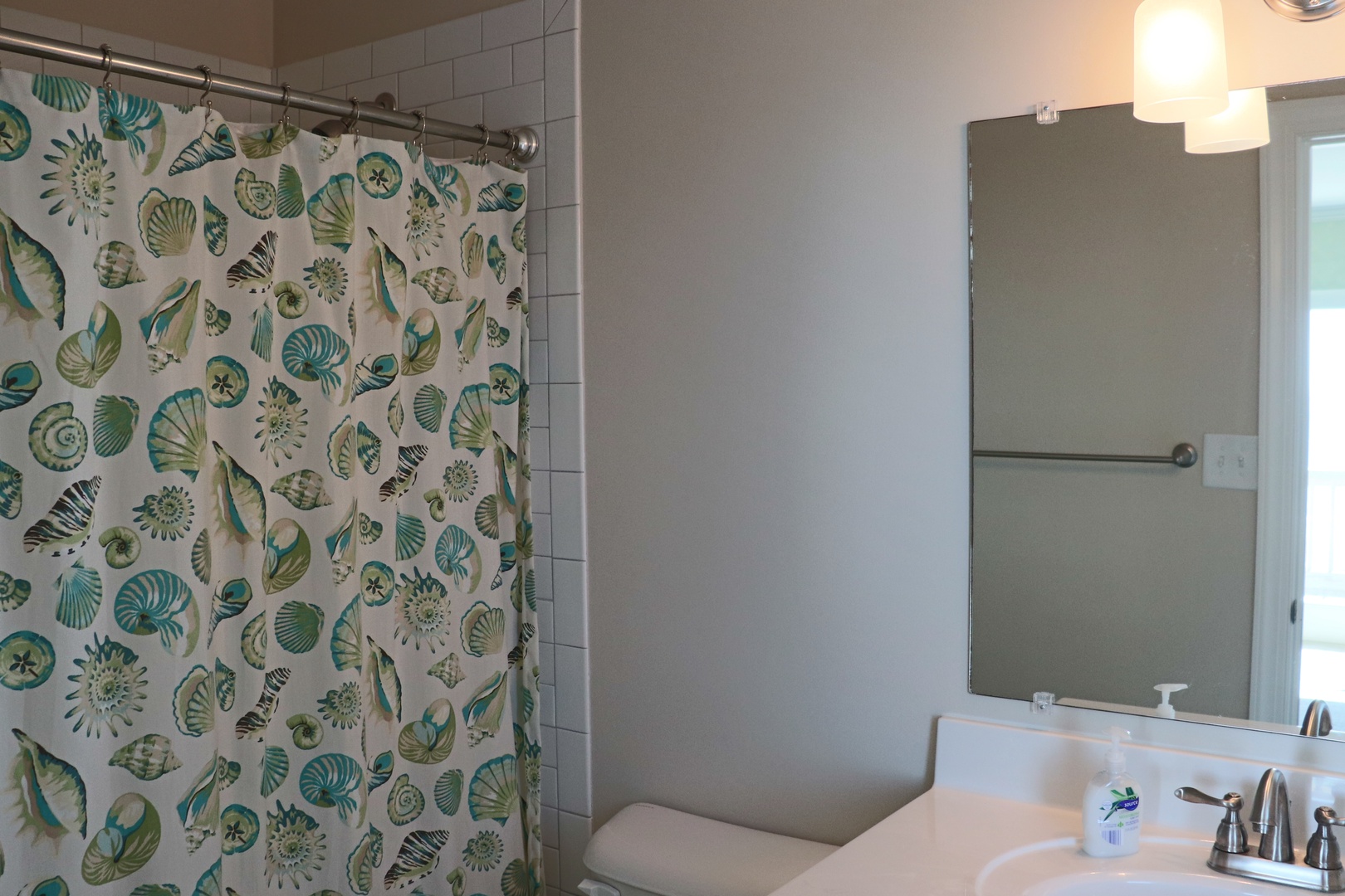 Step into your refreshing bathroom featuring a coastal-themed shower curtain and well-lit vanity area for your morning routine.