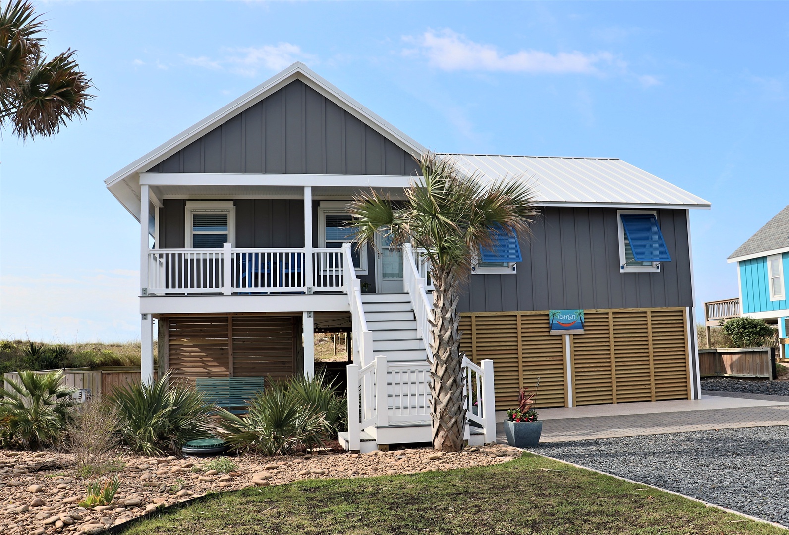 Charming coastal beach house with tropical palm trees and modern design, featuring covered parking and private outdoor space.