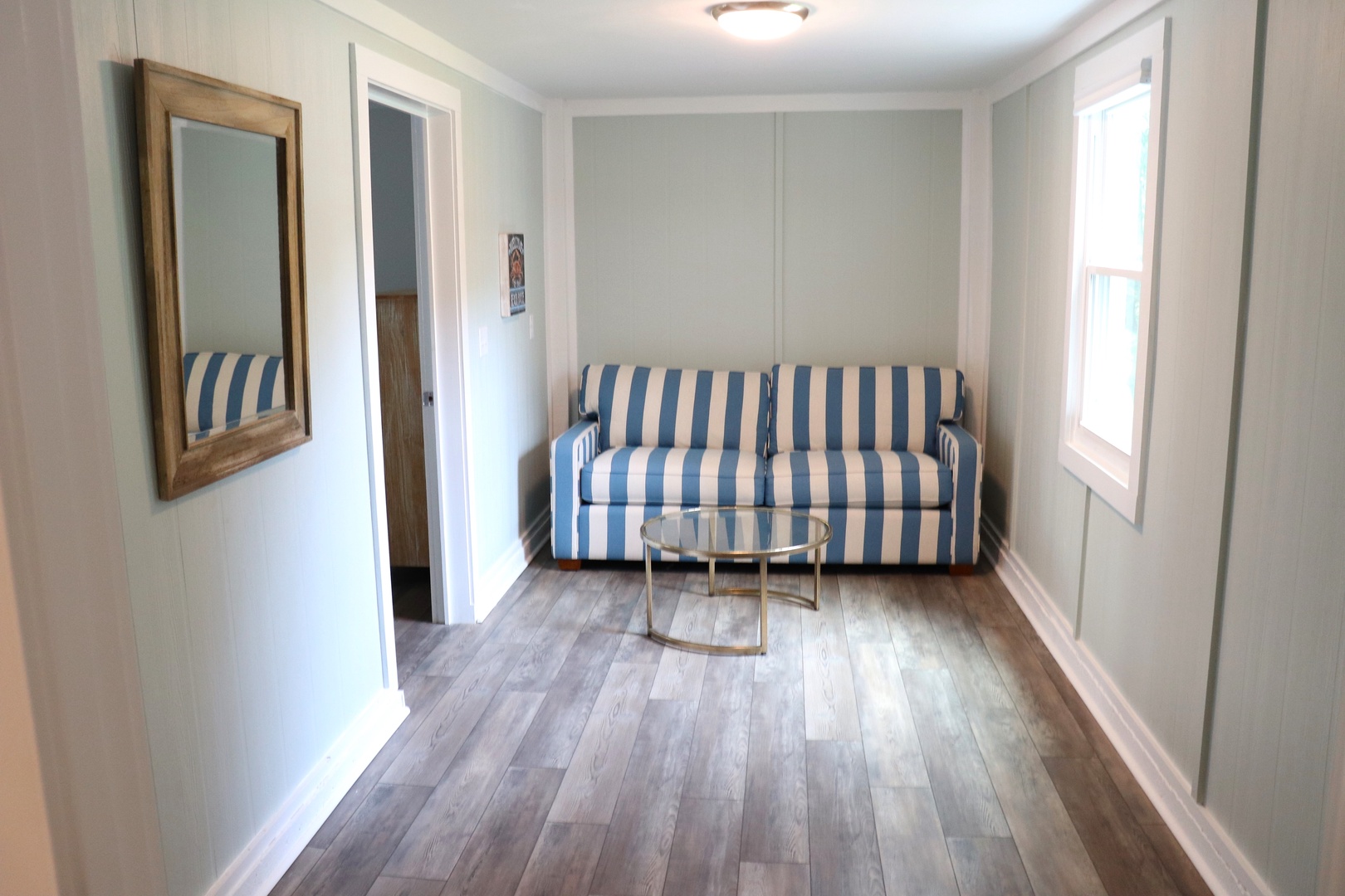 Relax on your charming blue-striped sofa in this bright, coastal-inspired living space with beautiful hardwood floors.
