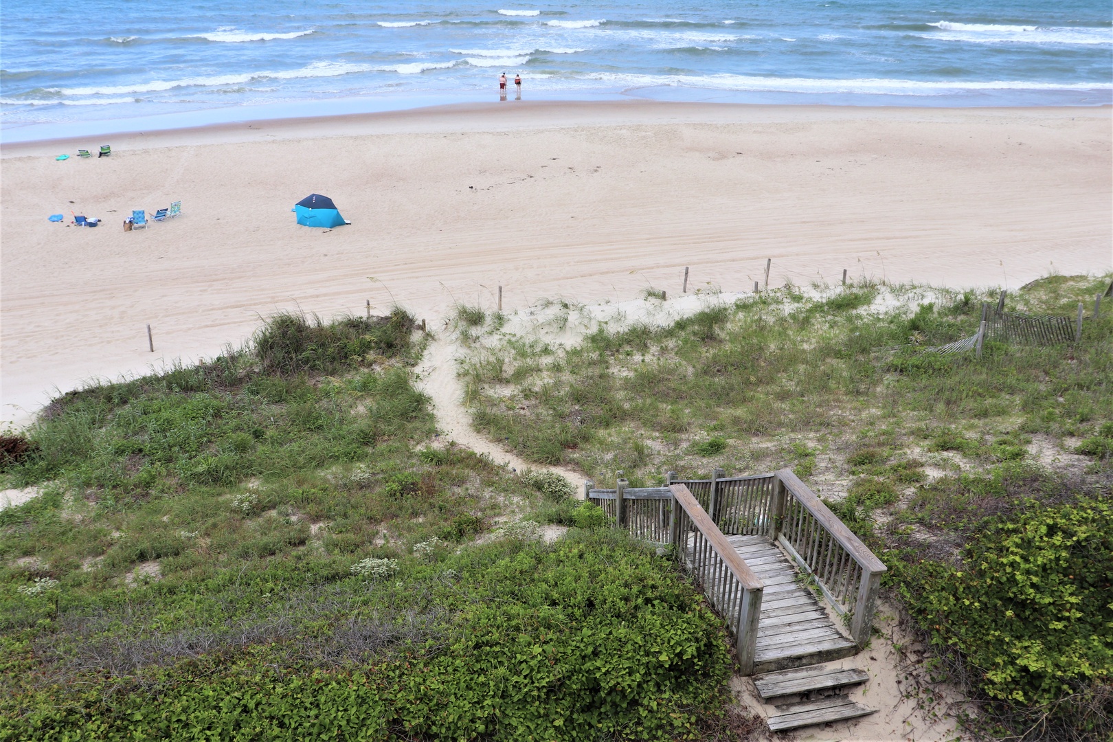 Beautiful sandy beach with gentle waves and natural dune vegetation. Wooden boardwalk provides easy access to pristine shoreline for beach activities.