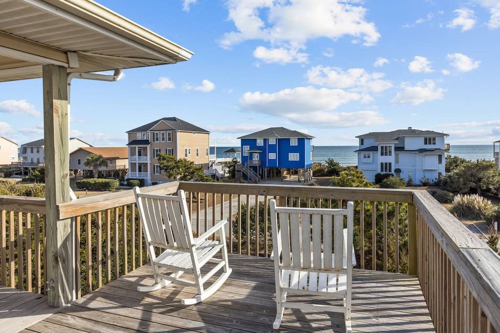 Peaceful deck with comfortable rocking chairs overlooking colorful beach houses and ocean views.