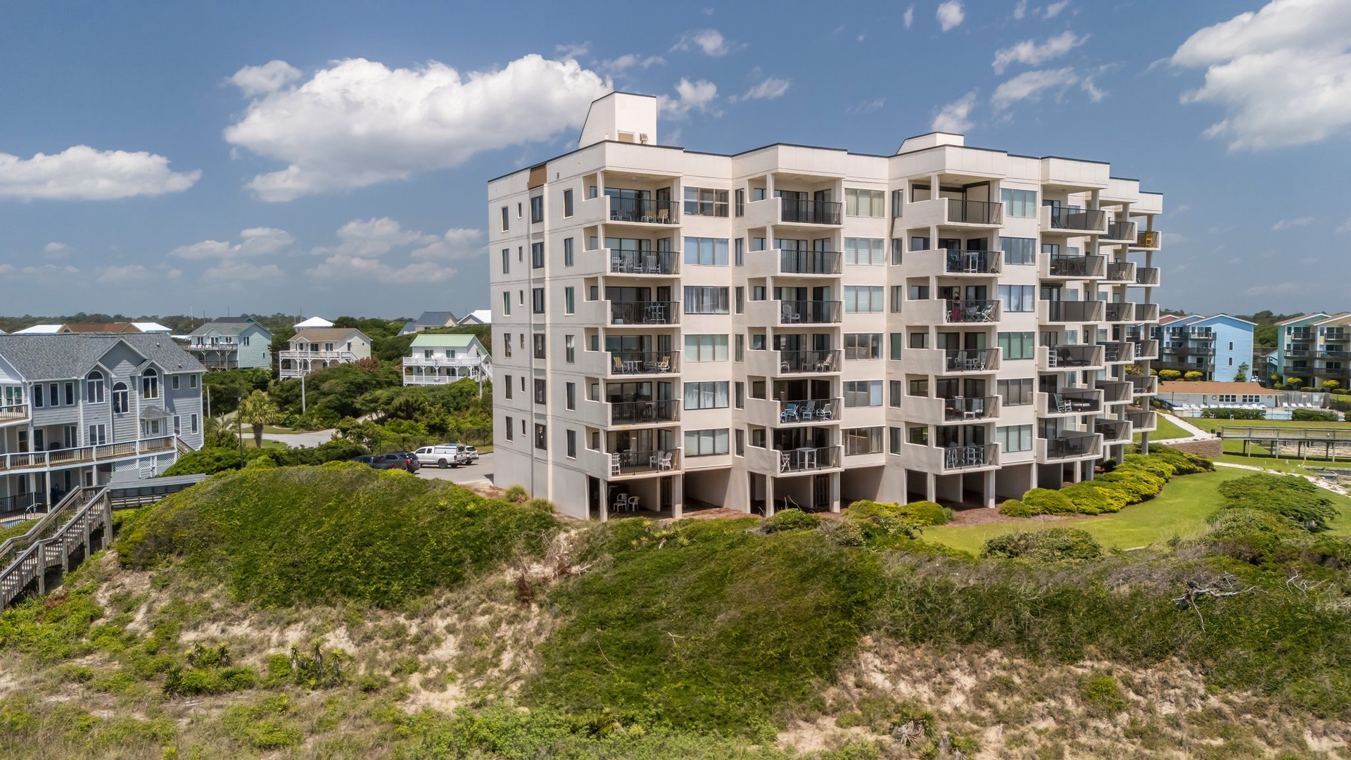 Modern beachfront condominium complex nestled among coastal dunes with multiple balconies overlooking the surrounding residential neighborhood.