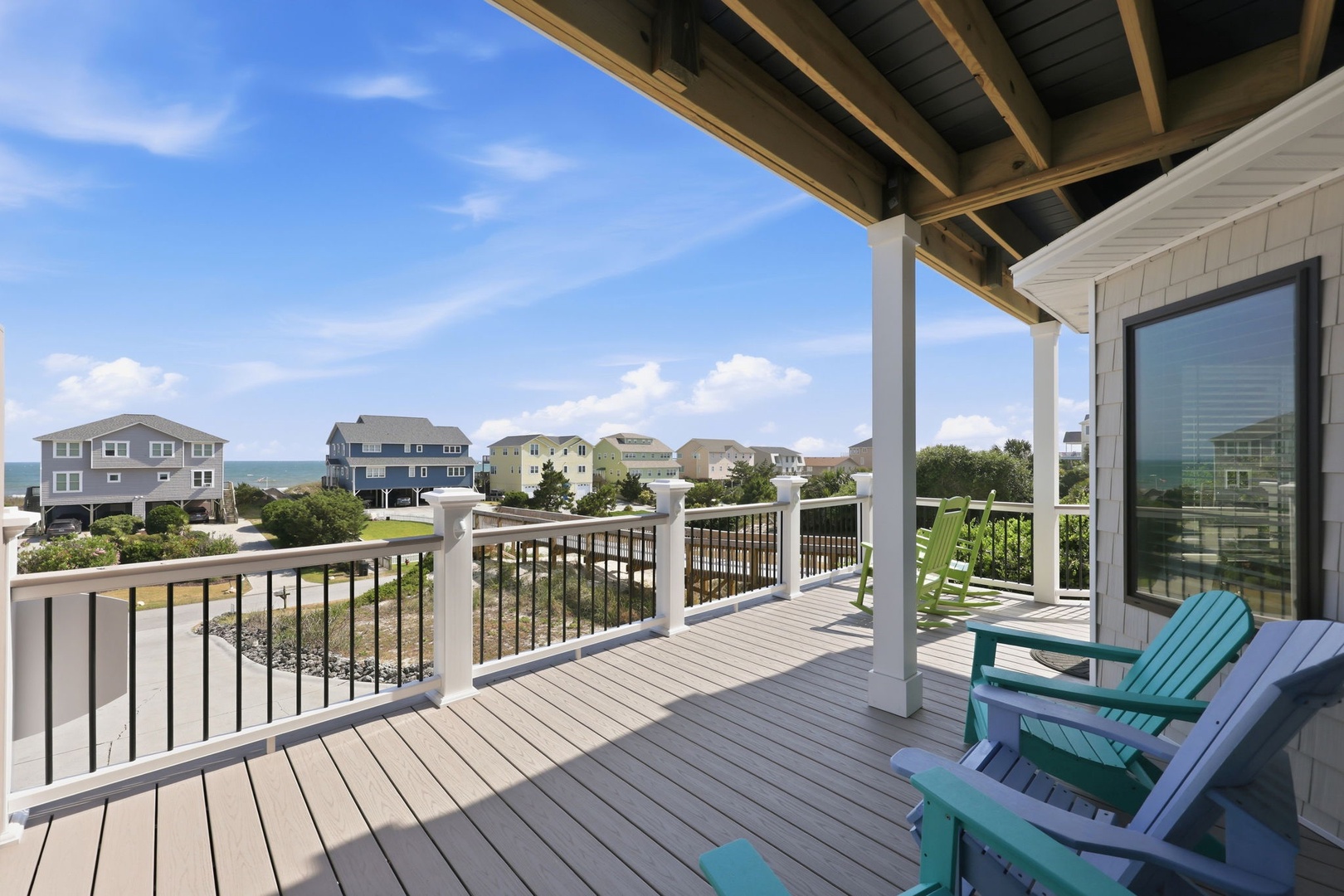 Covered deck overlooking a coastal neighborhood with partial ocean views, offering a breezy spot to relax in classic Adirondack chairs and savor the seaside setting.