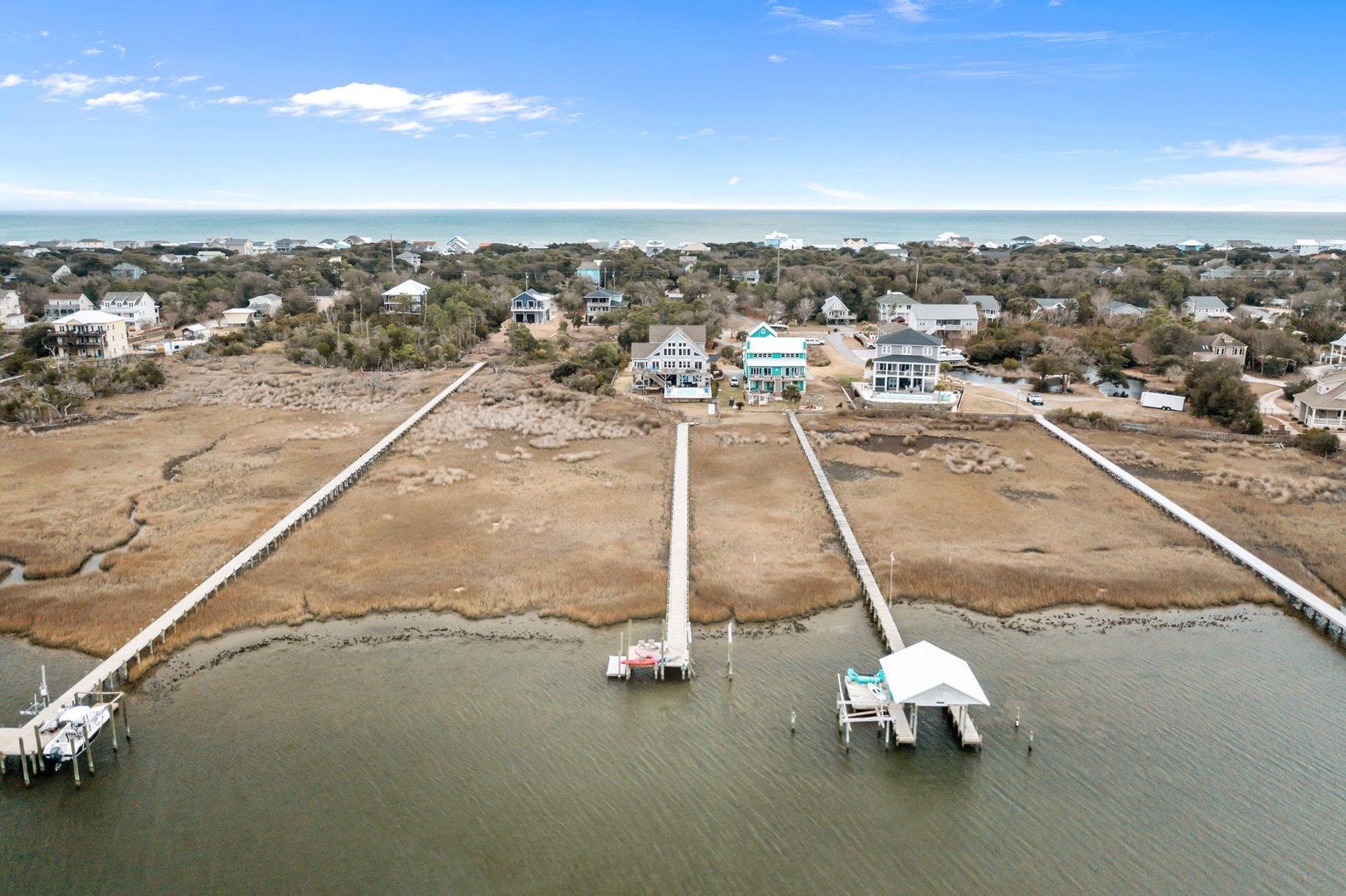 Aerial view showcases the coastal community with wooden boardwalks extending over marsh waters and vacation homes nestled among native vegetation.