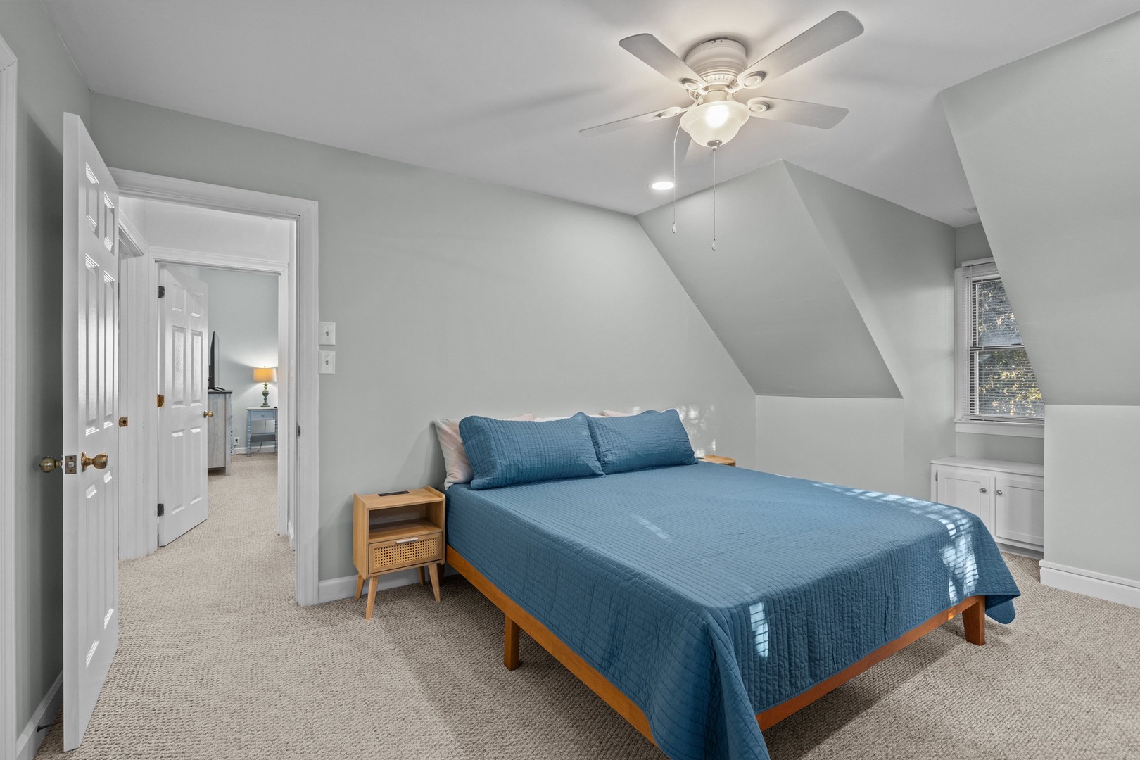 Unwind in your peaceful attic bedroom with soaring ceilings, cozy blue linens, and gentle ceiling fan breeze.