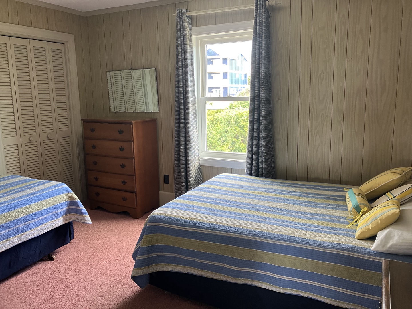 Relax in your cozy nautical-themed bedroom with twin beds, charming striped linens, and wood-paneled walls that create a peaceful coastal retreat atmosphere.