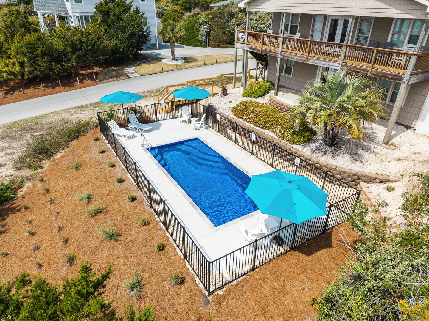 Aerial view of the property showcasing a private swimming pool with safety fencing, sun umbrellas, and coastal vacation homes in a quiet residential setting.