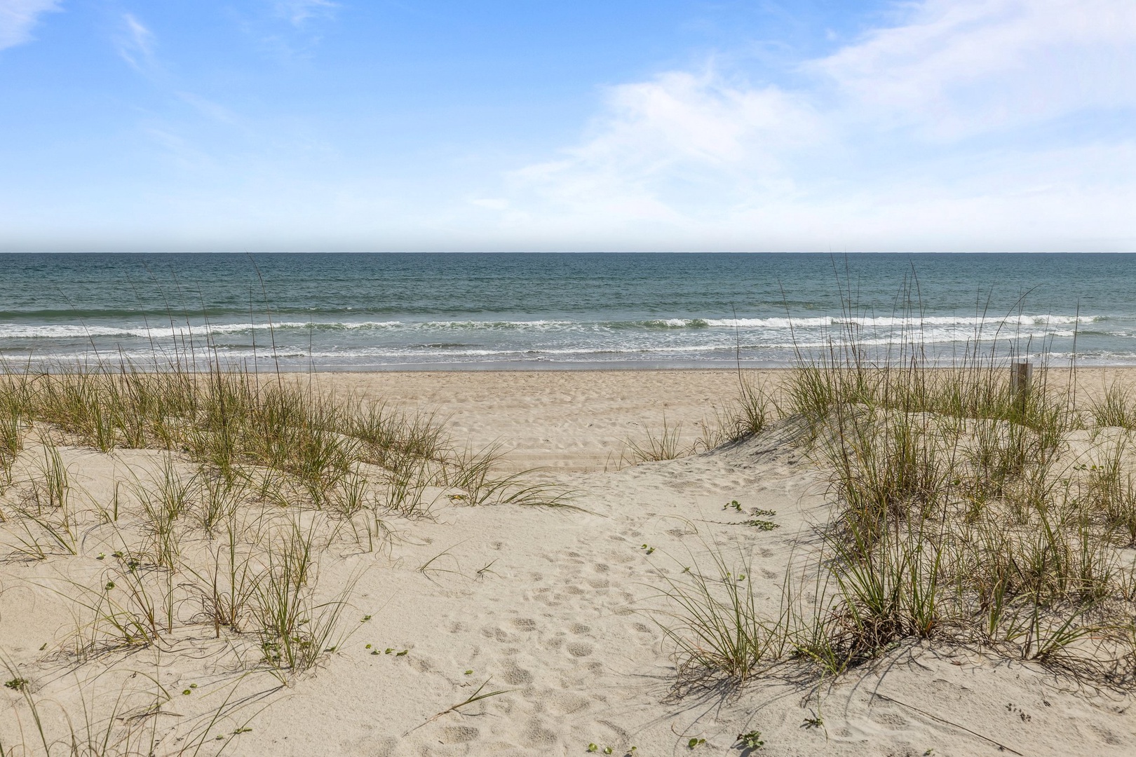 Pristine coastal beach with natural dunes and sea grass, offering direct ocean access and gentle rolling waves.