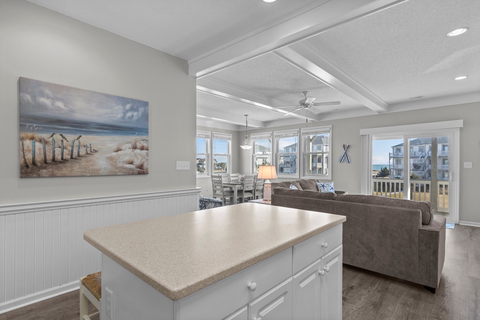 Your open-concept space flows seamlessly from kitchen island to cozy living room, with coastal artwork setting the mood.
