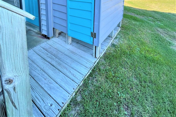 Step onto your private deck surrounded by lush green lawn, where weathered wood planks lead to bright blue shutters framing your peaceful retreat.