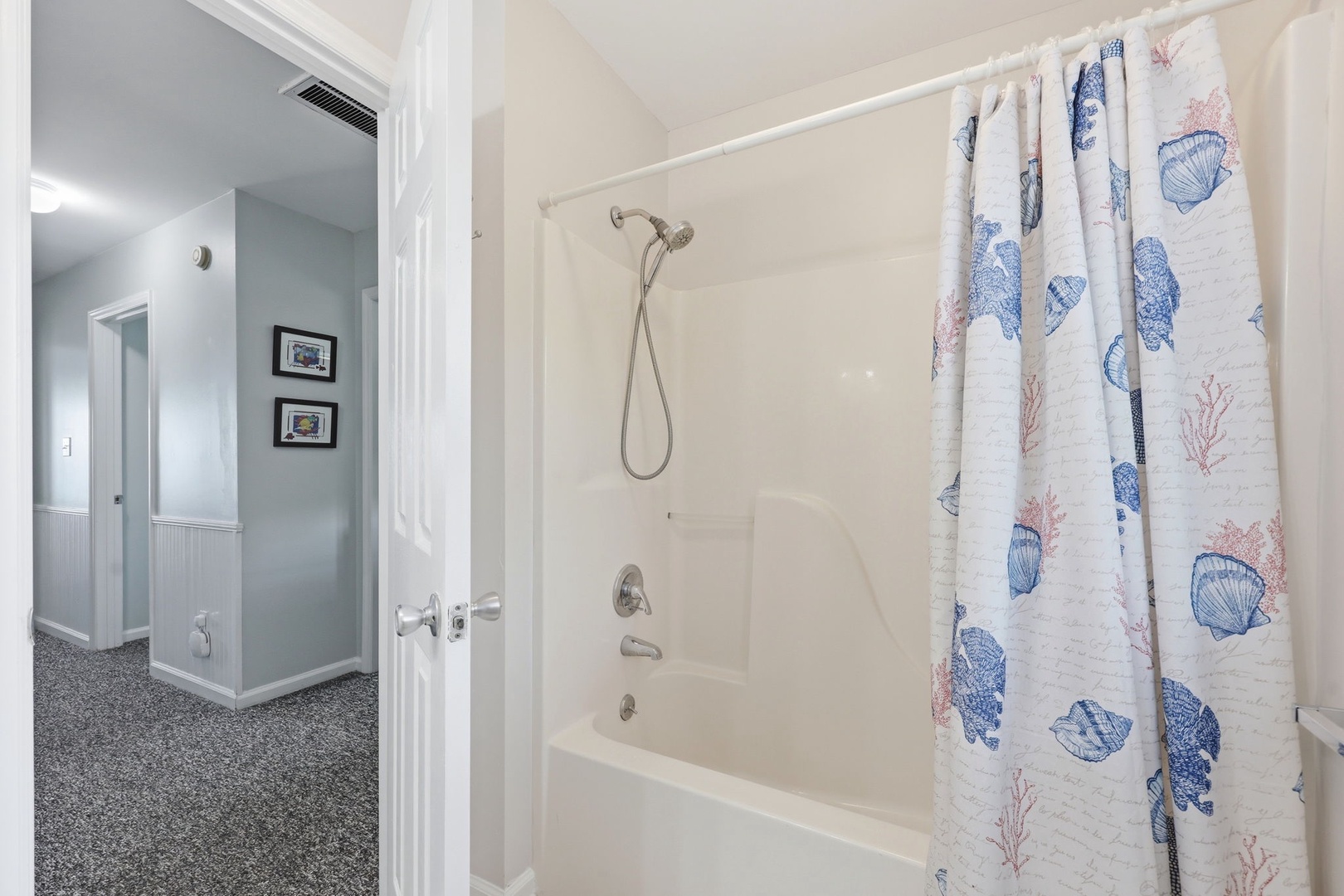 Step into your pristine bathroom featuring a full tub-shower combo with coastal-inspired seashell curtains. Bright, clean, and ready for your arrival.