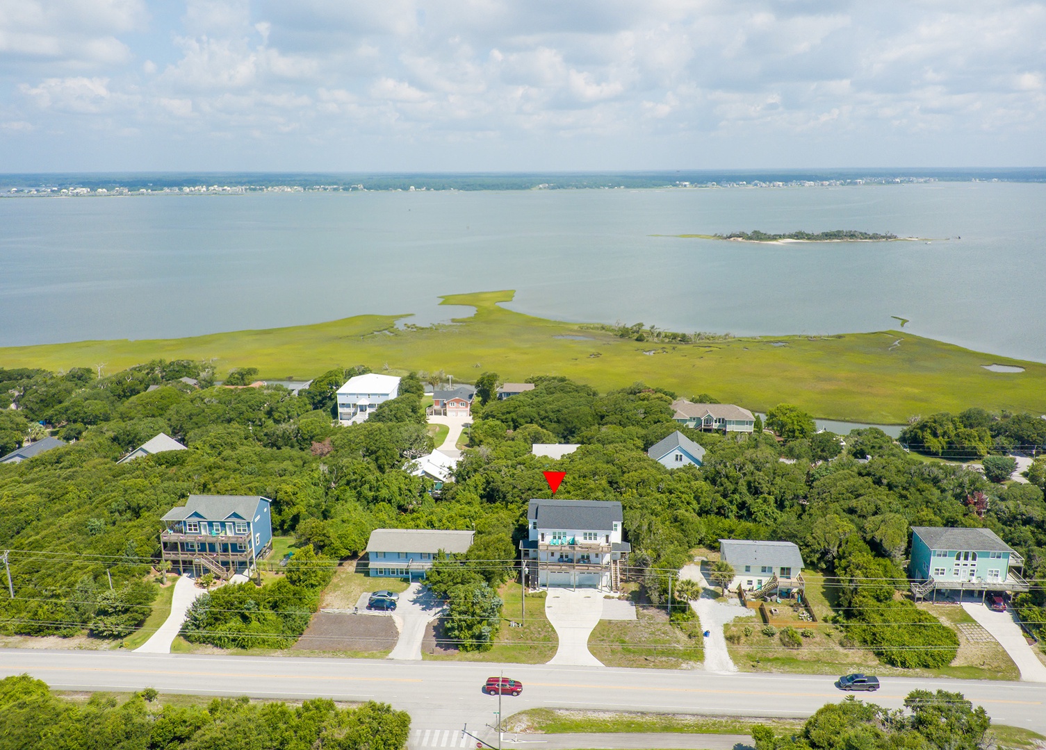 Aerial view of waterfront community with homes nestled among mature trees near pristine bay waters and salt marshes.