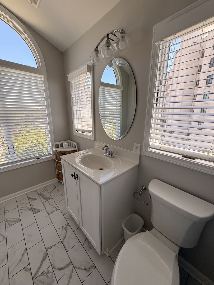Bright, modern bathroom with marble-style tile, large soaking tub, and natural light streaming through skylight and windows. Fresh white finishes and plush towels await your arrival.