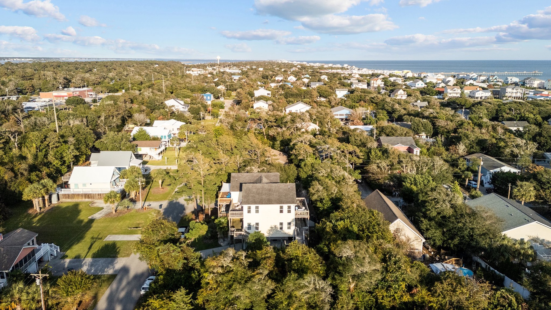 Aerial view of a charming coastal neighborhood with tree-lined streets and homes nestled among lush greenery near the waterfront.