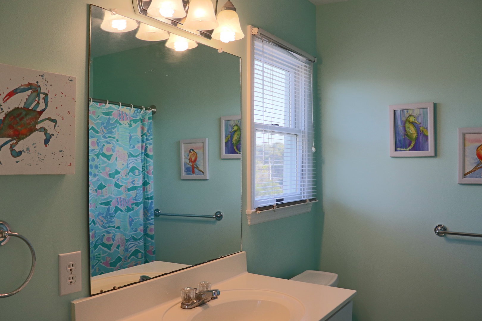 Your fresh, ocean-inspired bathroom awaits with vibrant artwork and natural light streaming through.