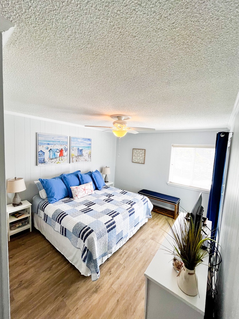 Your cozy coastal bedroom features crisp blue and white linens, cheerful beach art, and natural light streaming through windows for peaceful nights.